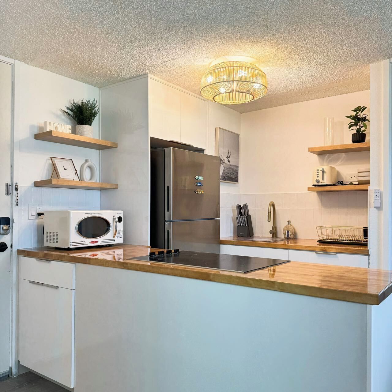 Une cuisine moderne avec des meubles blancs, un réfrigérateur en acier inoxydable, un four à micro-ondes et des plans de travail en bois.