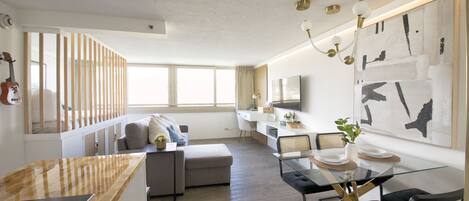 A modern living space with a dining area, a sofa, a TV, and a guitar on the wall.