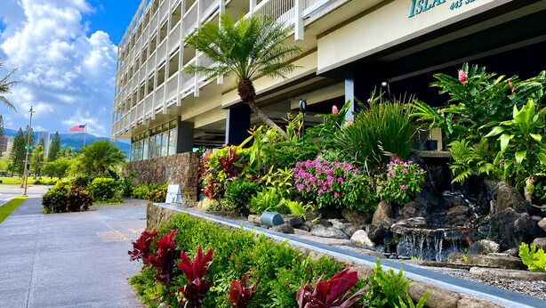 A hotel with a name sign, a stone facade, and a landscaped area with plants and a small waterfall. - Honolulu Central Waikiki luxury High With Views & Beach (Honolulu)