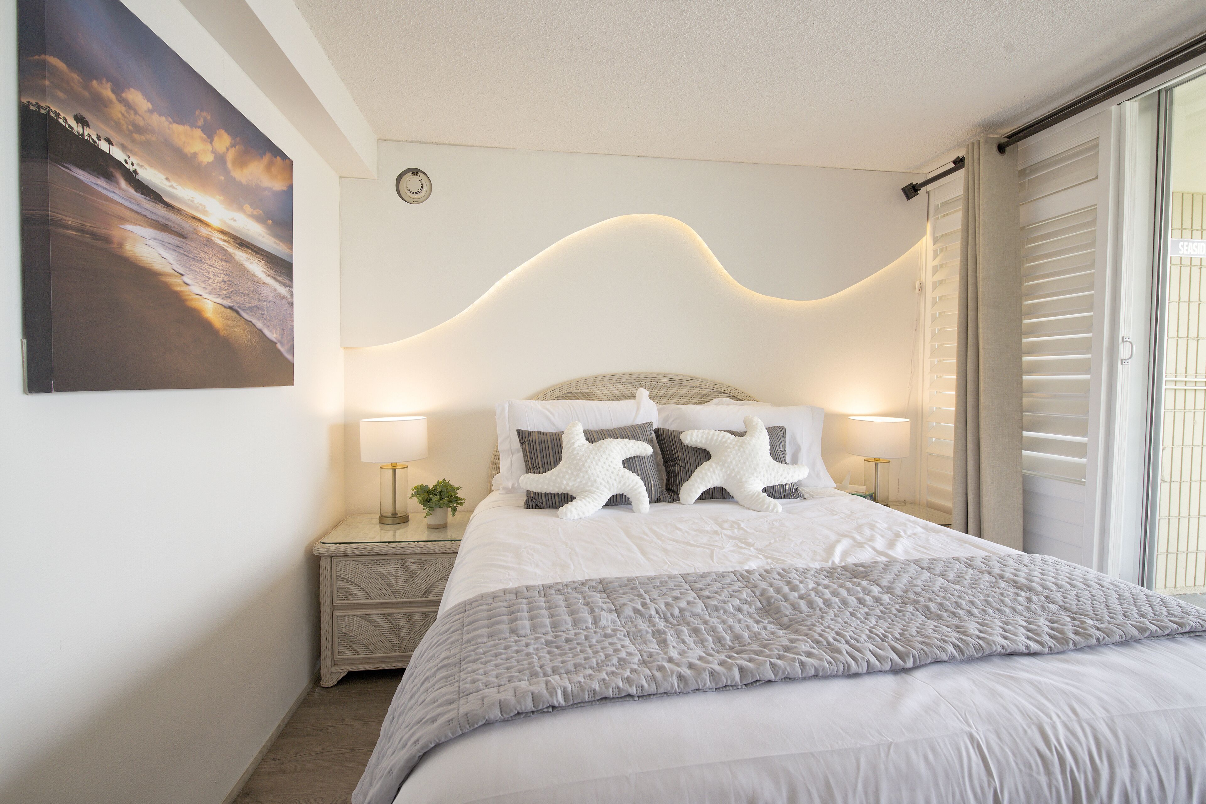 A neatly made bed with a white and gray quilt, two bedside lamps, and a starfish pillow.