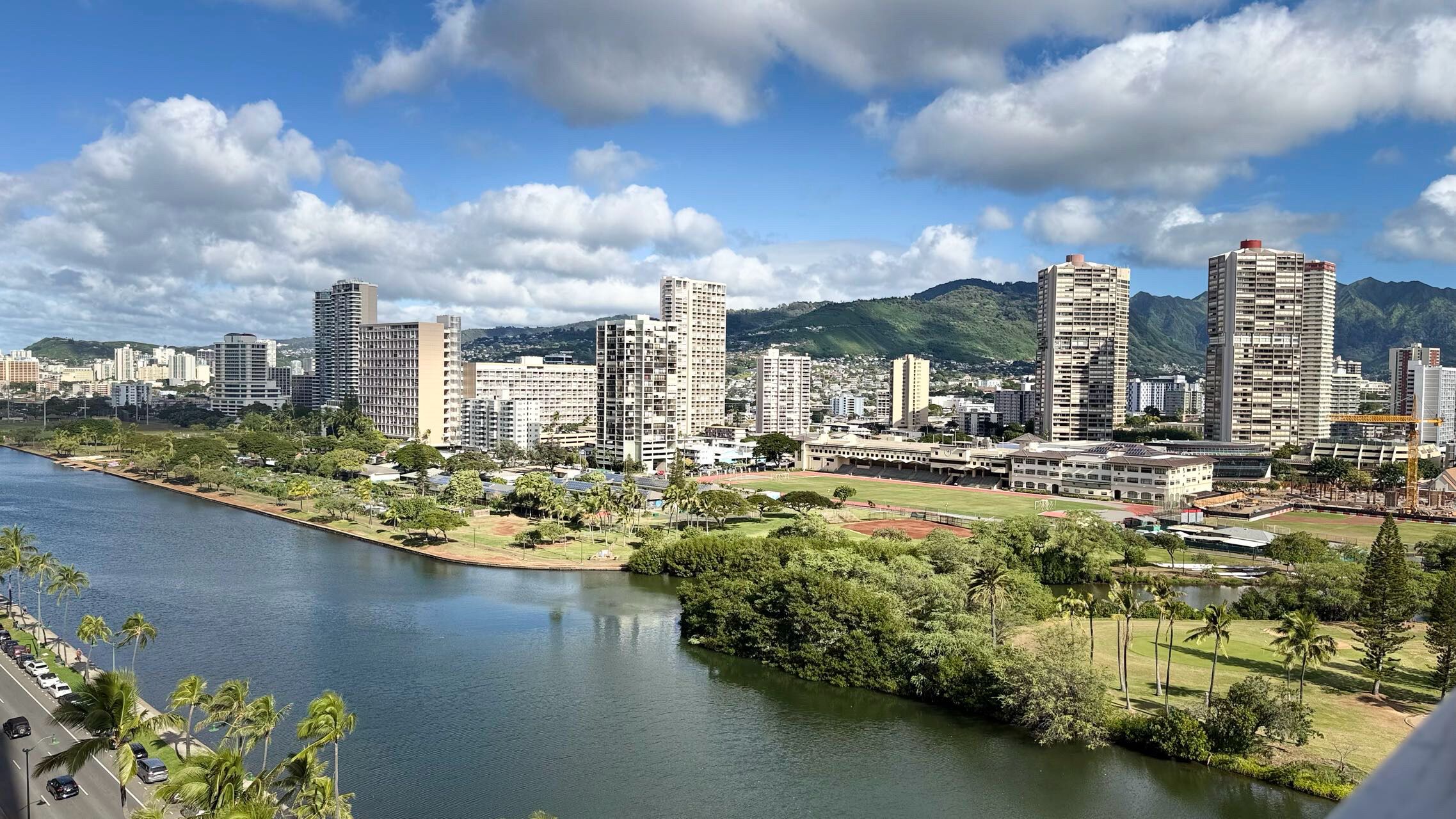 A cityscape with high-rise buildings, a river, and a park with palm trees.