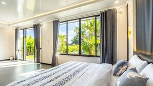 Ein modernes Hotelzimmer mit einem großen Bett, Vorhängen und Blick auf Grünfläche.