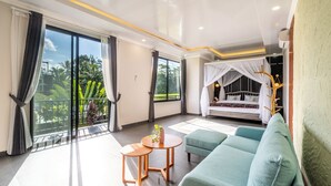 Ein geräumiger Raum mit einer großen Glasschiebetür, die auf einen Balkon führt, einem Himmelbett, einem grünen Sofa und einem kleinen runden Tisch.