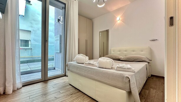 Un dormitorio moderno con una cama grande, un ventanal corredero a un balcón y un diseño minimalista.