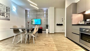 Una cocina moderna con horno empotrado, un comedor con mesa y sillas de madera, y un televisor de pantalla plana montado en la pared.