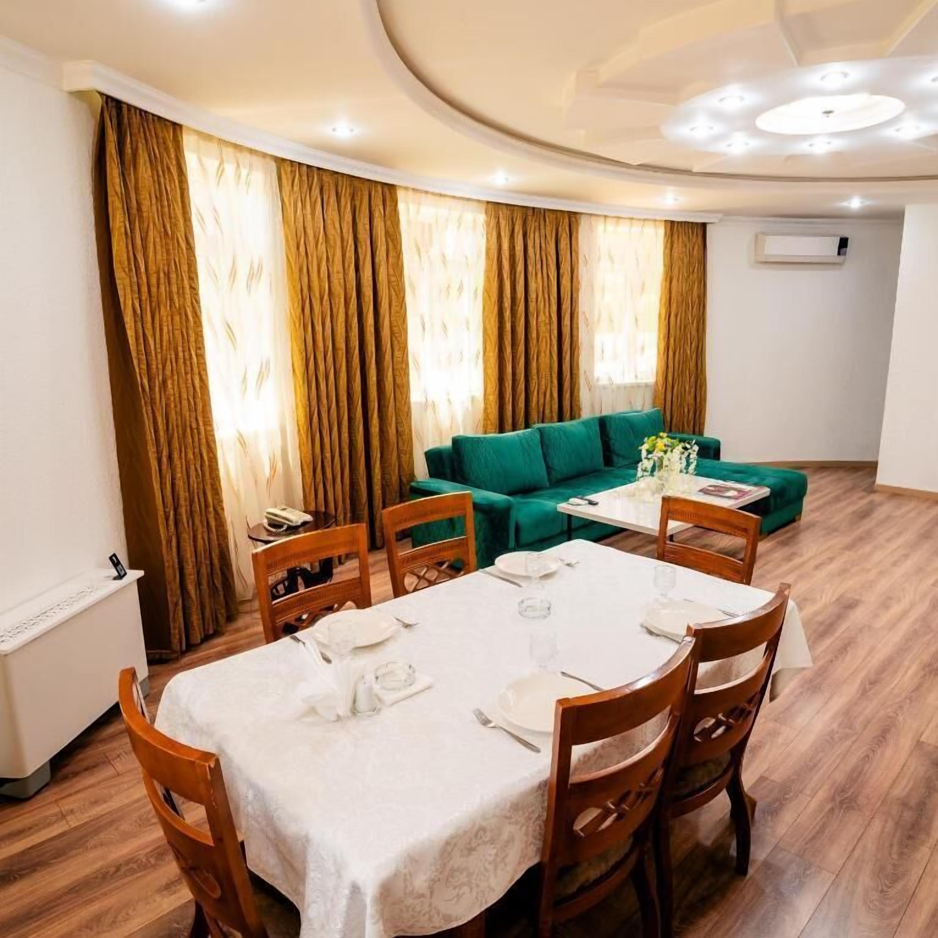 A dining area with a table set for four, a green sofa, and a window with curtains.
