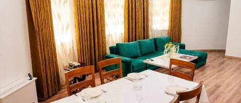 A dining area with a table set for four, a green sofa, and a window with curtains.