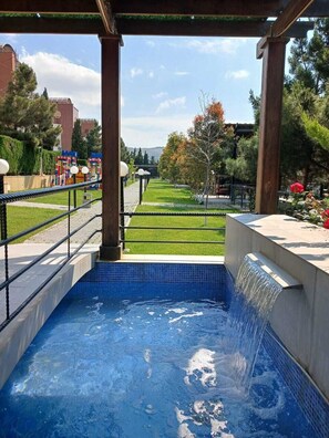 A swimming pool with a water feature, surrounded by a garden and a pergola structure. - Panorama Villa Lux  (Baku)