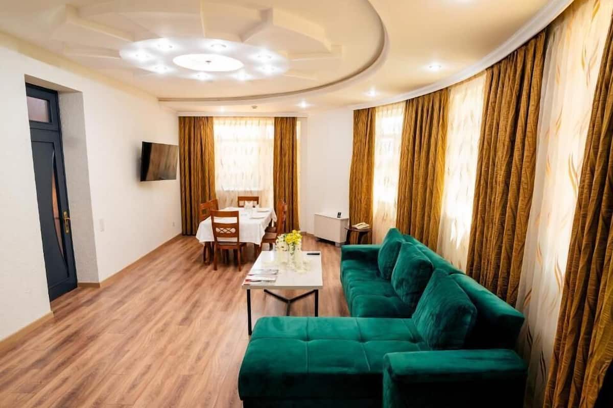A living room with a green sofa, a dining area with a table and chairs, and a TV mounted on the wall.
