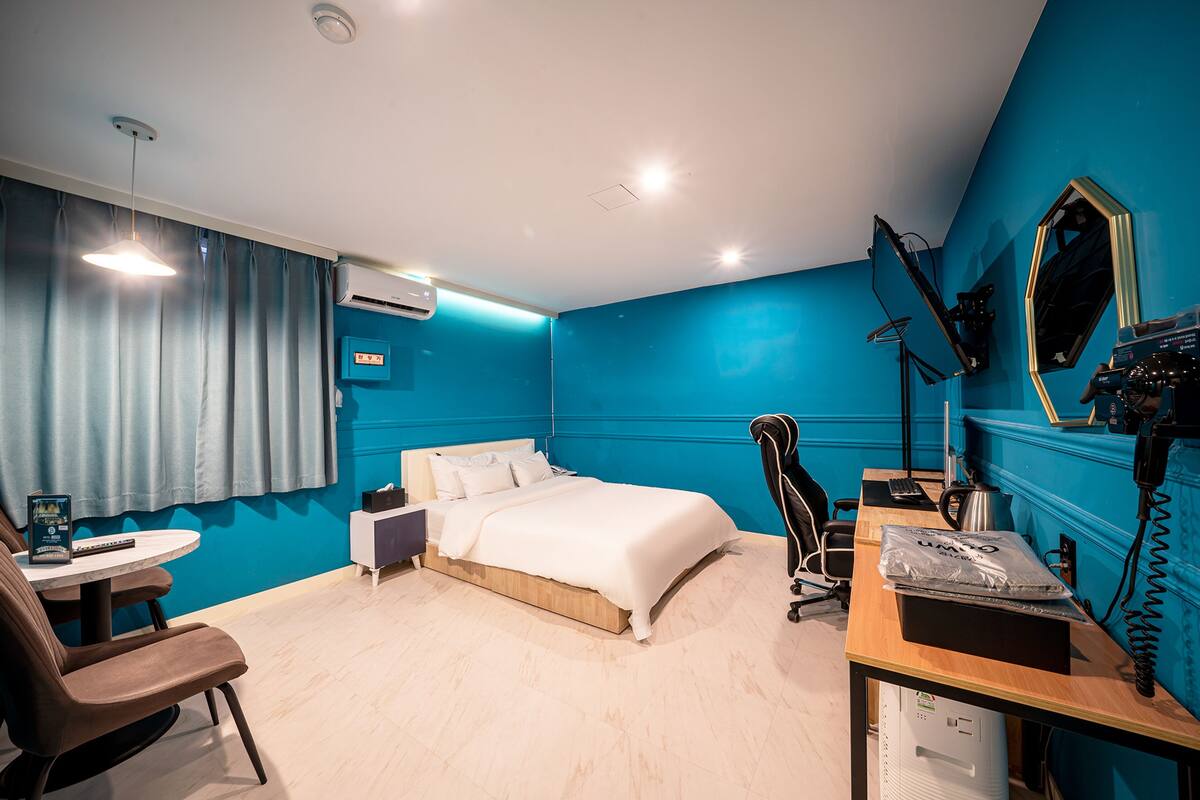 A modern hotel room with a large bed, a desk with a computer, a chair, and a TV.