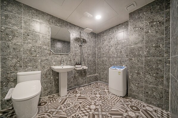 A bathroom with a toilet, sink, and shower. The walls are tiled with a speckled pattern, and the floor has a geometric tile design. - Hotel Bosco Incheon (Incheon)