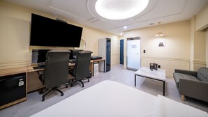 A modern hotel room with a large flat-screen TV, a desk with two office chairs, a small refrigerator, a sofa, and a round ceiling light. - Hotel Bosco Incheon (Incheon)