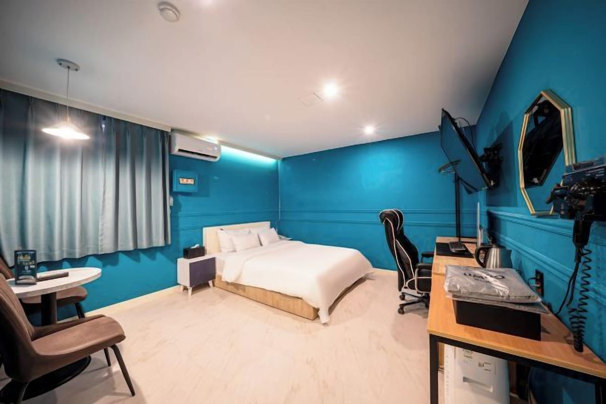 Una habitación de hotel con cama, escritorio, silla y un espejo en la pared.