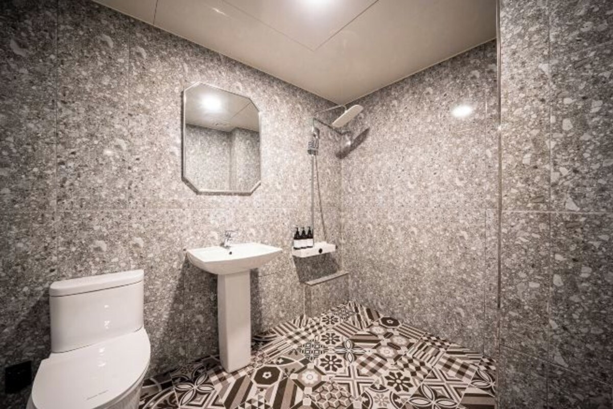 A bathroom with a toilet, sink, and shower. The walls are covered in a speckled tile pattern.
