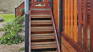A wooden staircase leading to a covered porch with a view of a river and trees in the background. - Riverside chalet in Aviemore, short walk to centre (Aviemore)
