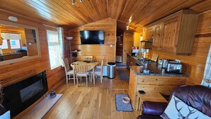 A cozy cabin interior with wooden walls, a dining area with chairs and a table, a kitchen with a stove and cabinets, and a fireplace. - Riverside chalet in Aviemore, short walk to centre (Aviemore)