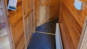 A narrow hallway with wooden walls and doors, a blue carpet, and a radiator on the right. - Riverside chalet in Aviemore, short walk to centre (Aviemore)