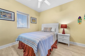 A bedroom with a bed, a nightstand, a ceiling fan, and two framed pictures on the wall. - San Carlos 1908 (Gulf Shores)
