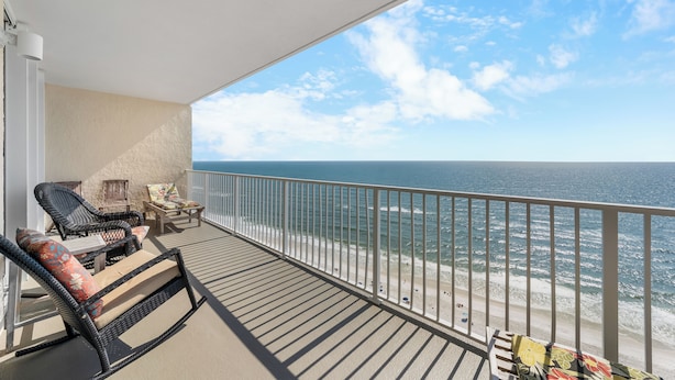 Ein Balkon mit Korbstühlen und einem Tisch, mit Blick auf Strand und Meer.