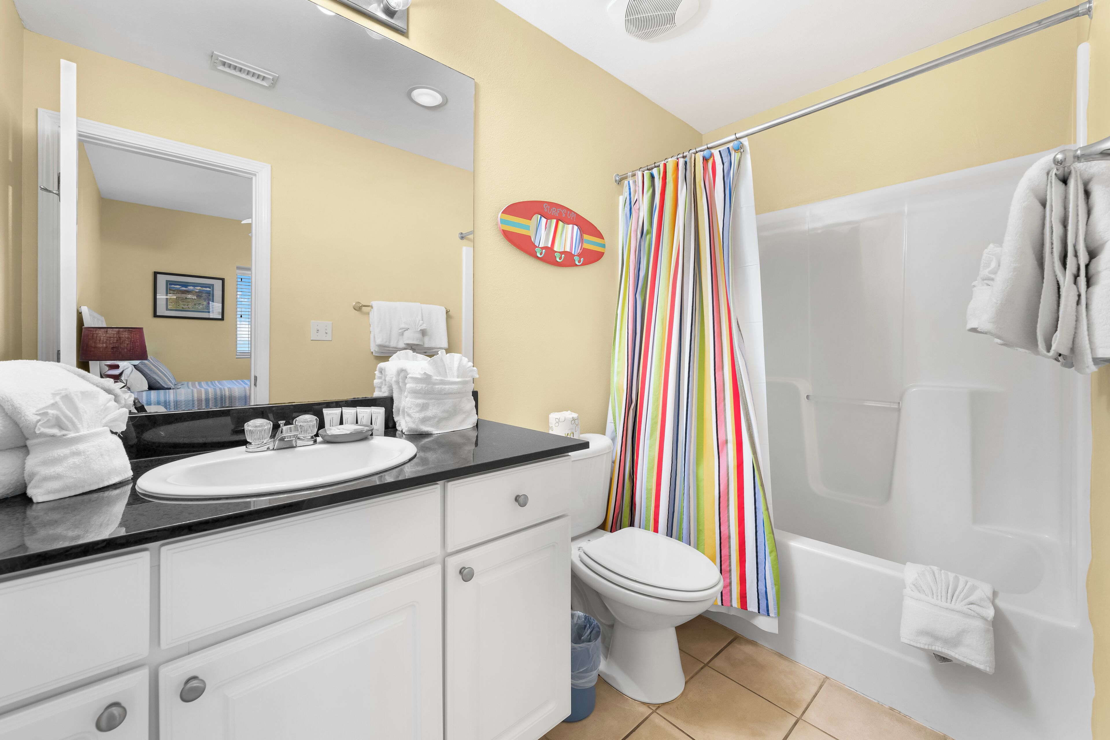 Ein Badezimmer mit weißem Waschbecken, WC und Badewanne. Ein gestreifter Duschvorhang und ein Handtuchhalter mit Handtüchern sind vorhanden.