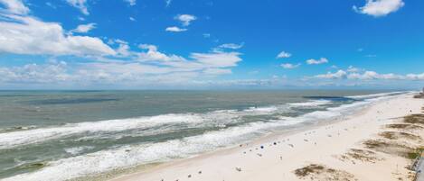 Ein Strand mit breitem Sandstrand, sanften Wellen und blauem Himmel.