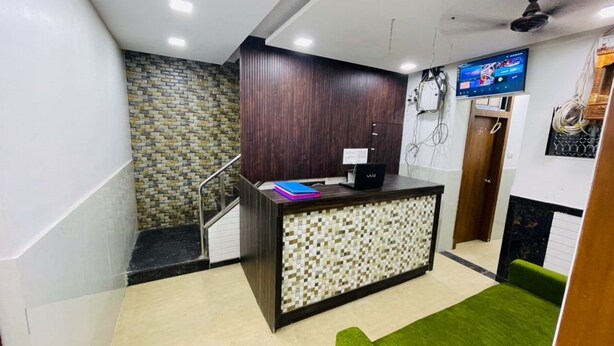 A reception area with a reception desk, a television, and a green sofa. - HOTEL RADHA PALACE (Mumbai)