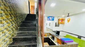 A staircase with a brick wall on one side and a reception desk with a green couch on the other. - HOTEL RADHA PALACE (Mumbai)