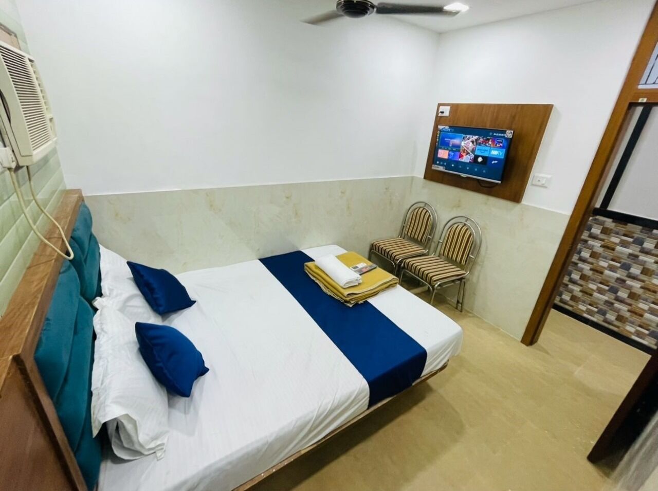 A hotel room with a bed, a TV mounted on the wall, and a ceiling fan.