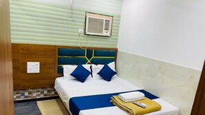 A small hotel room with a bed, a bedside table, a wall-mounted air conditioner, and a door. - HOTEL RADHA PALACE (Mumbai)