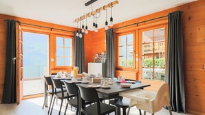 A dining area with a table set for six, surrounded by black chairs, a white high chair, and a wooden ceiling with hanging light fixtures.