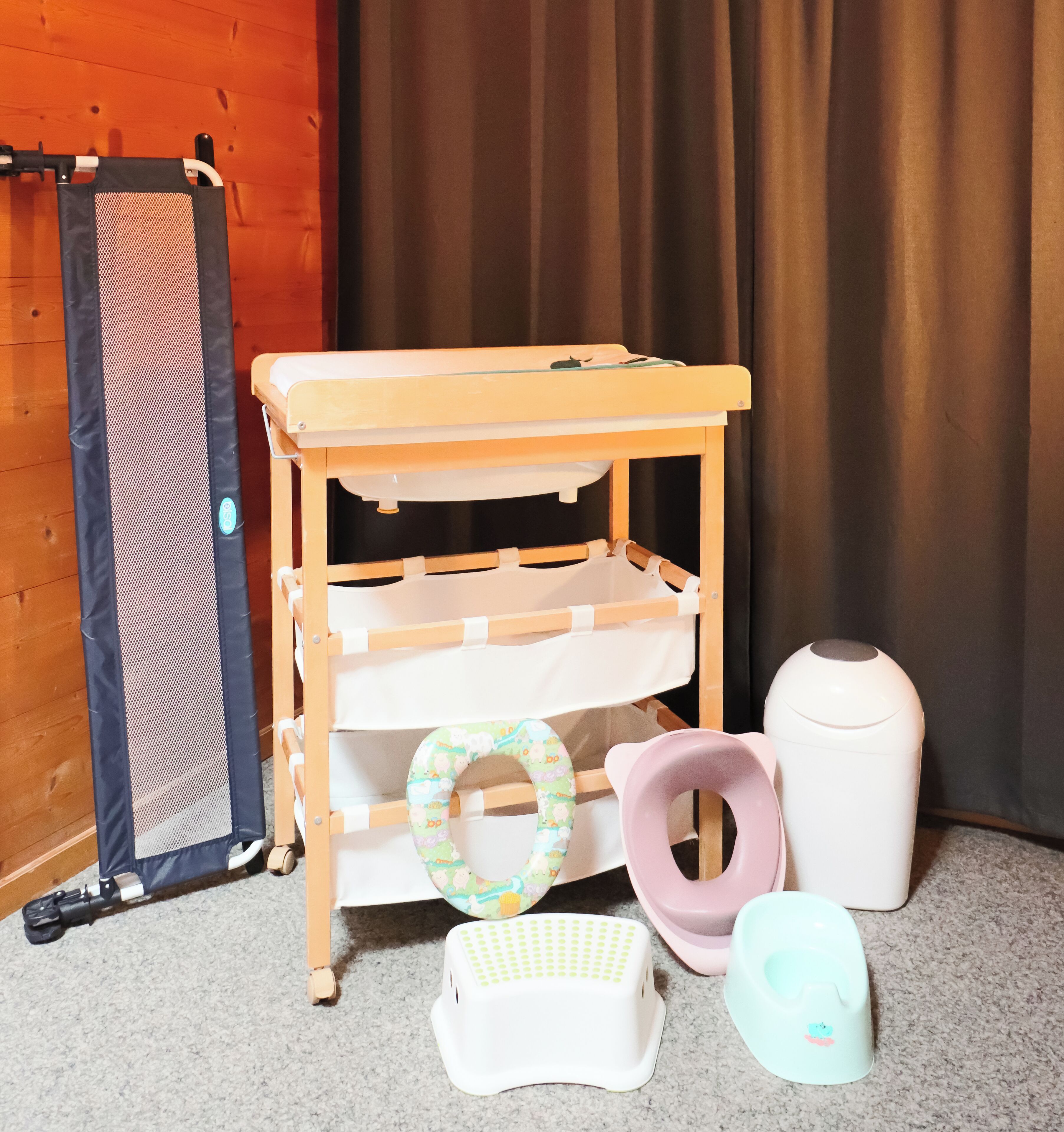 A wooden baby changing table with shelves, a baby seat, and a diaper pail.