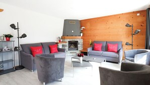 A modern living room with grey sofas, red cushions, a stone fireplace, and a wooden accent wall.