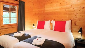 A wooden cabin-style room with a large bed, red and white bedding, and a nightstand with a lamp.