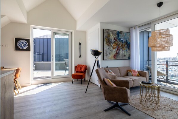 Ein modernes Wohnzimmer mit einer Couch, einem Sessel, einer Stehlampe und einem großen Fenster mit Blick auf die Stadt.