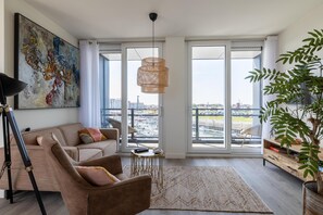 Ein modernes Wohnzimmer mit Sofa, Sesseln, Couchtisch und einem großen Fenster mit Blick auf die Stadt.