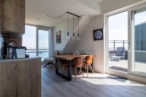 Eine moderne Küche mit Holzarbeitsplatte, ein Essbereich mit Holztisch und Stühlen sowie eine große Schiebeglasdoor, die auf einen Balkon führt.