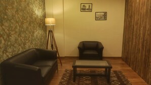 Une pièce comprenant un canapé en cuir noir, un fauteuil noir, une petite table, un lampadaire et deux tableaux encadrés accrochés au mur.