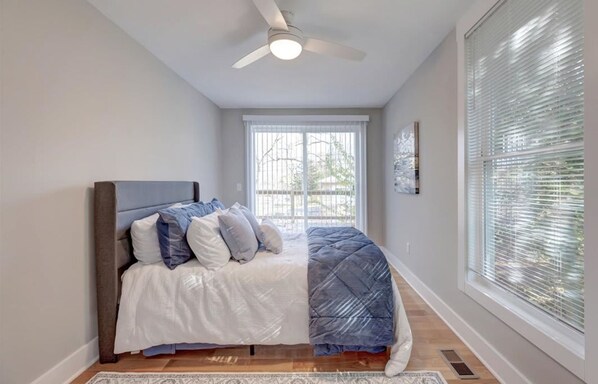 Une chambre à coucher avec un lit, un ventilateur de plafond, une fenêtre avec des stores et une porte.
