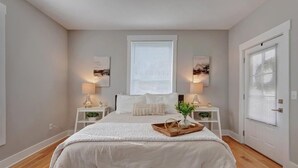 A bedroom with a large bed, bedside tables with lamps, a window with blinds, and a door with a window.