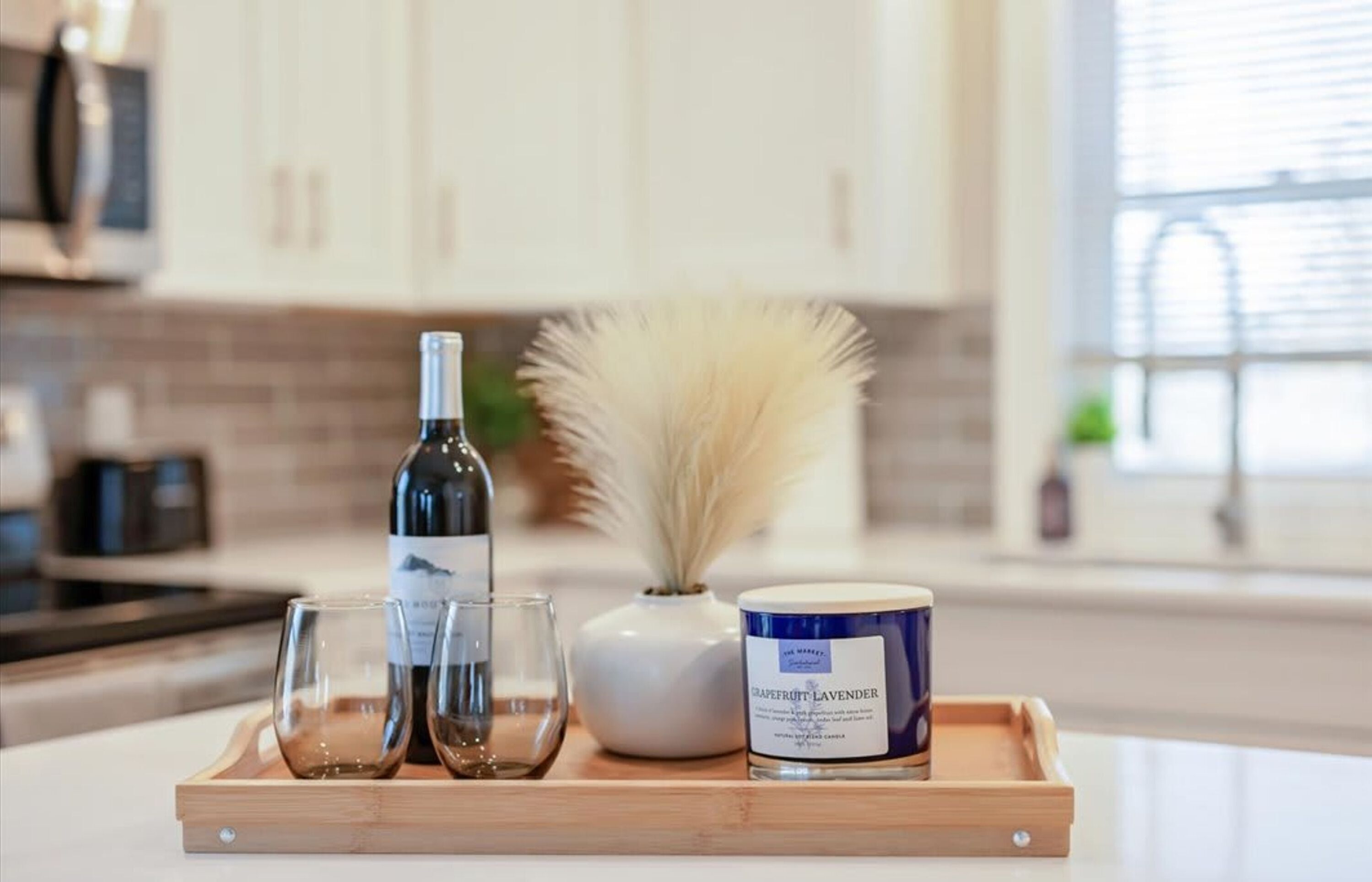 A tray with a bottle of wine, two glasses, a vase with white flowers, and a candle labeled "GRAPEFRUIT LAVENDER".