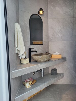 A modern bathroom with a stone sink, a black faucet, a wall-mounted mirror, and a towel on the left.