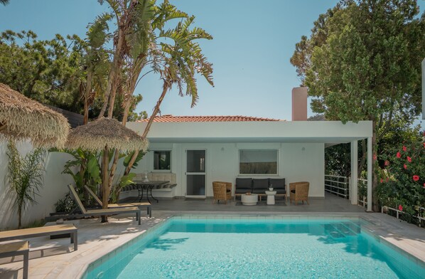 A modern house with a swimming pool, outdoor seating, and tropical plants.