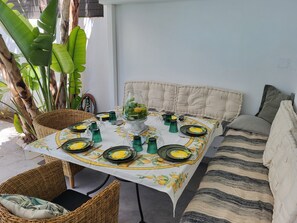 A dining table set with plates, glasses, and a centerpiece, surrounded by wicker chairs and a sofa.
