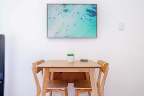 Een eethoek met een houten tafel en stoelen, een kleine plant in een pot en een lijst met een foto van een strand.