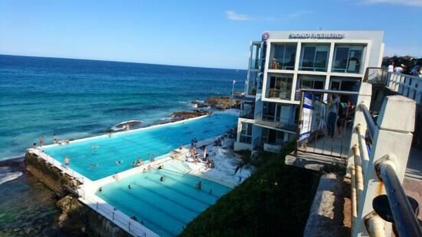 A hotel with a pool overlooking the ocean, a balcony with people, and a clear sky.