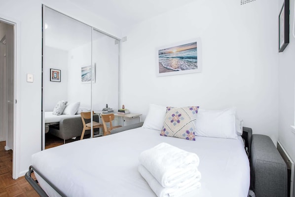 Habitación de hotel con cama, escritorio, silla, una mesita y un cuadro en la pared.