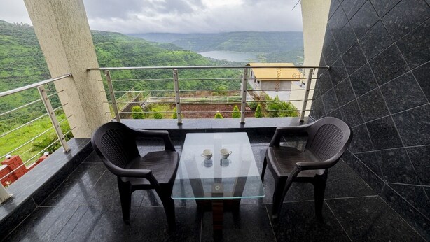Ein Balkon mit einem Glastisch und zwei Stühlen, mit Blick auf eine üppige grüne Landschaft und einen See.