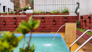 Ein Schwimmbecken mit Wasserspiel, umgeben von einer Ziegelmauer mit Blumentöpfen.