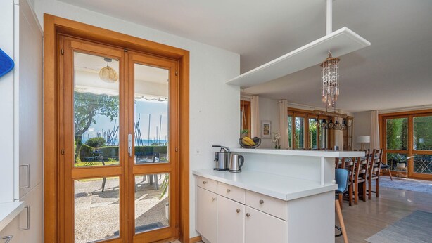 A modern kitchen with white cabinets, a wooden door, and a view of the outdoors. - Villa Azur on Lake Neuchâtel (La Grande Béroche)