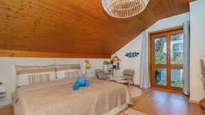 A bedroom with a large bed, a wooden ceiling, a window with curtains, and a small table with chairs. - Villa Azur on Lake Neuchâtel (La Grande Béroche)